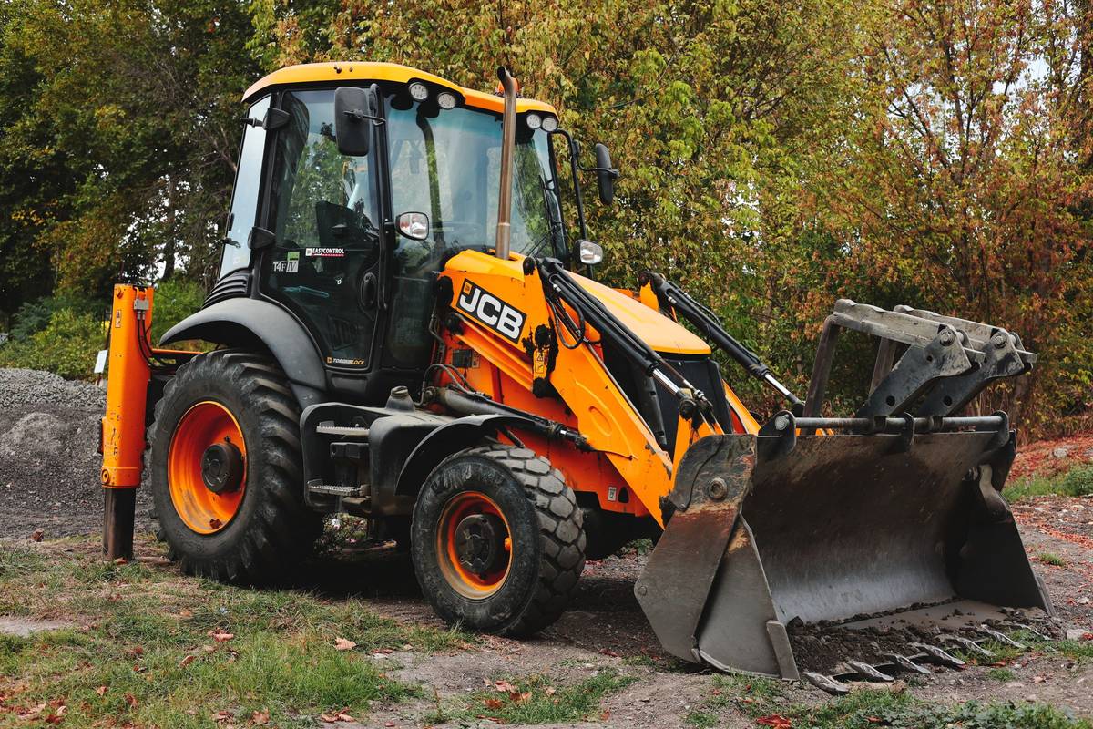 Backhoe loader parked on grass beside a stand of trees